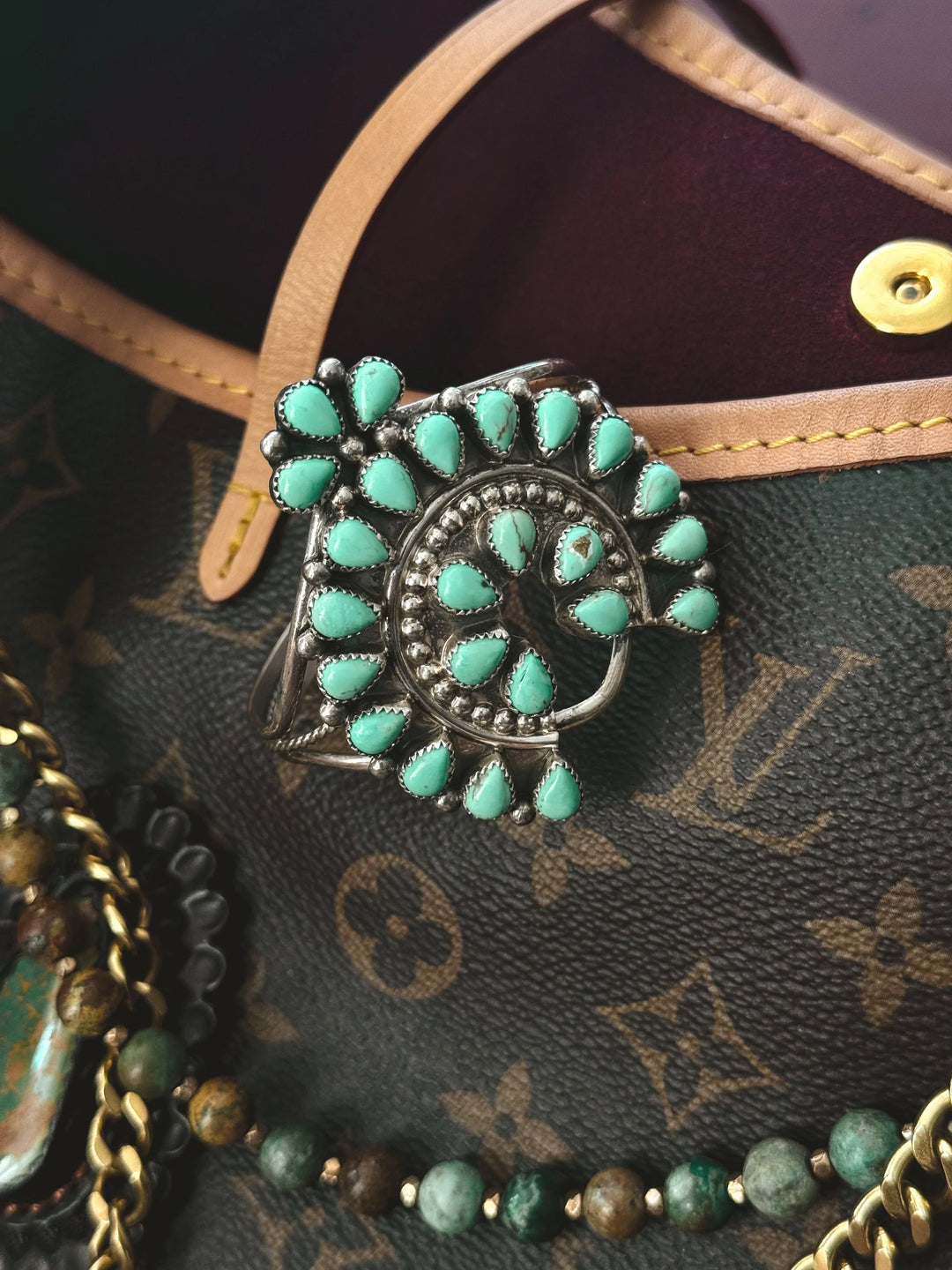 Turquoise western statement ring with silver setting on a leather designer bag surrounded by beaded jewelry.