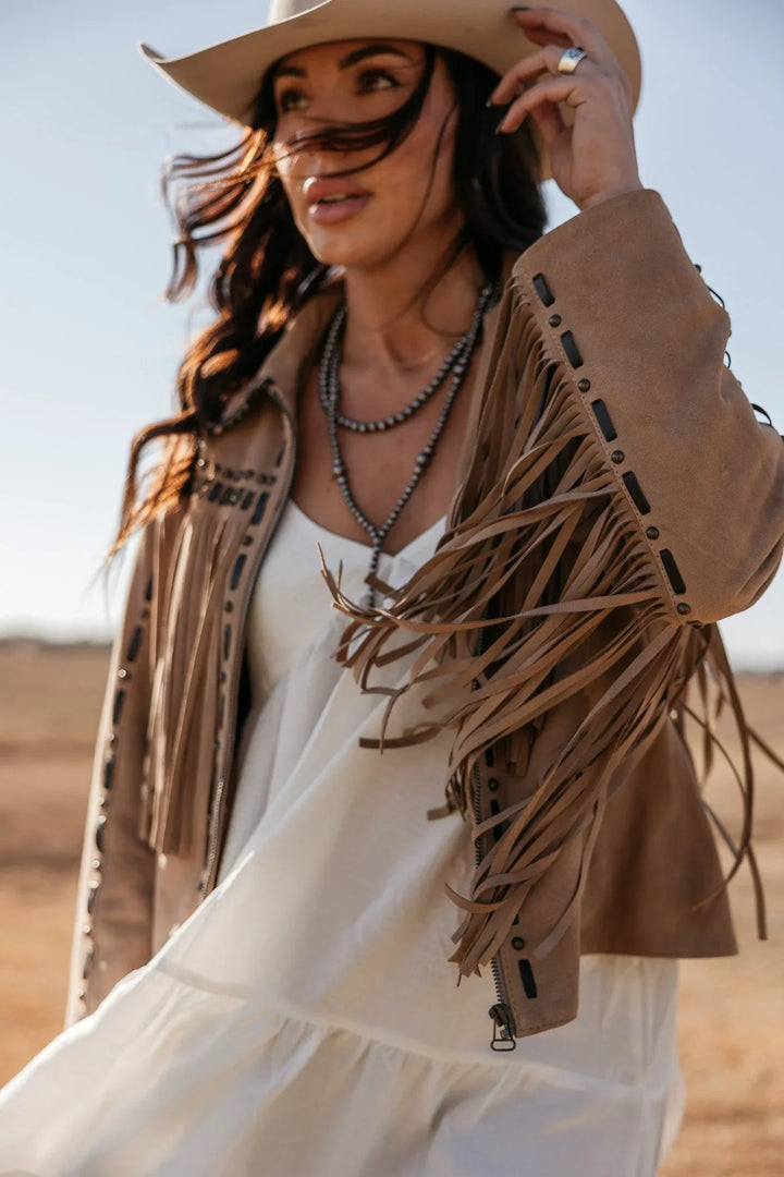Woman wearing a fringed jacket and cowboy hat in a desert setting