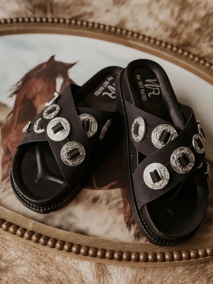 Black sandals with silver embellishments on a textured surface