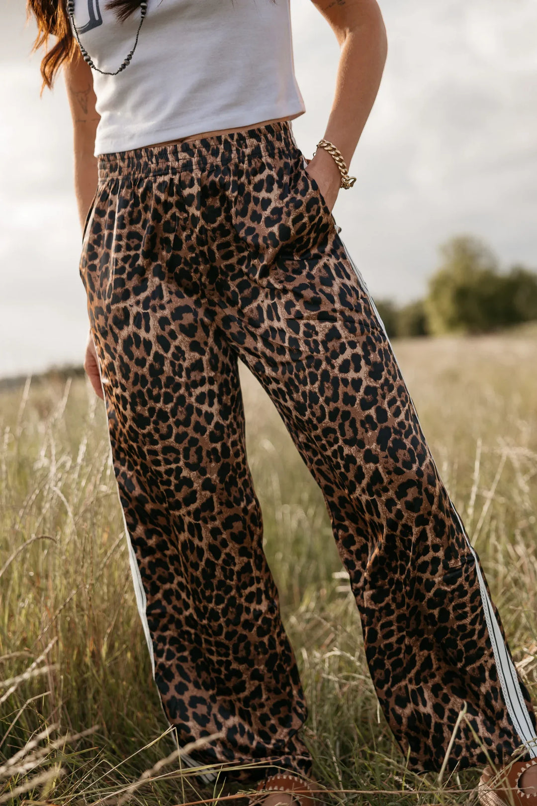 Person wearing leopard print pants with a white top in a grassy field.