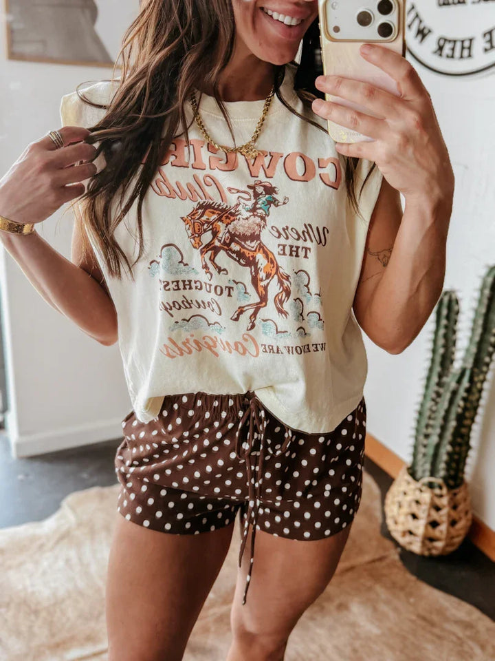 Woman wearing a graphic t-shirt and polka dot shorts taking a mirror selfie.