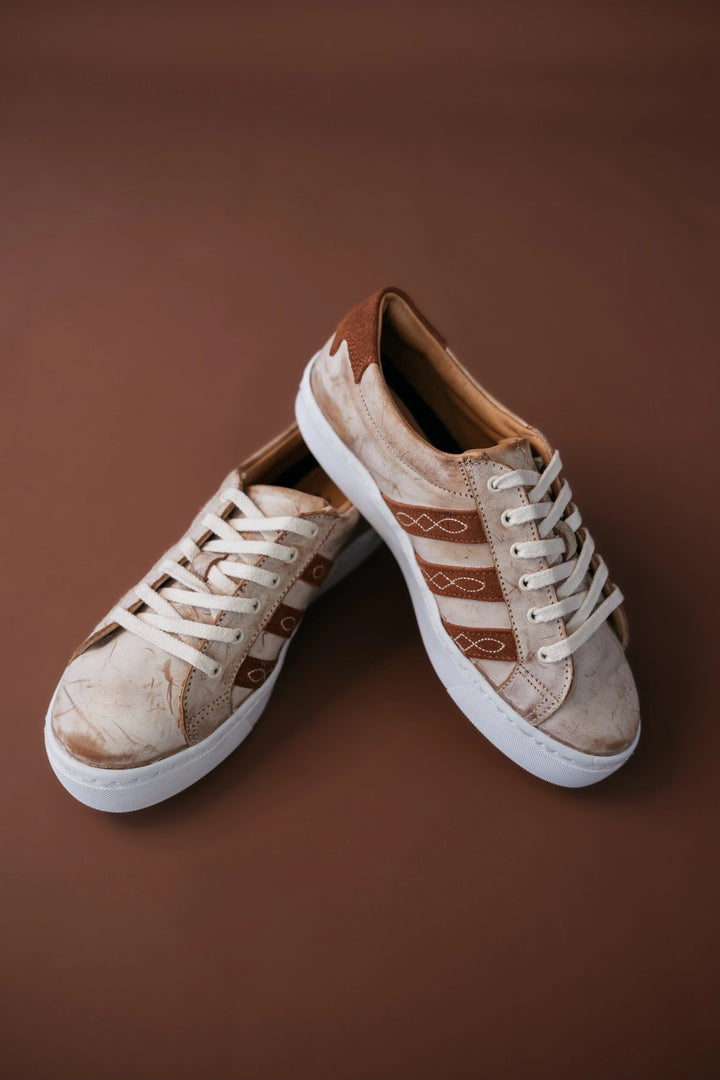 Western-inspired brown and tan sneakers with white laces on brown background