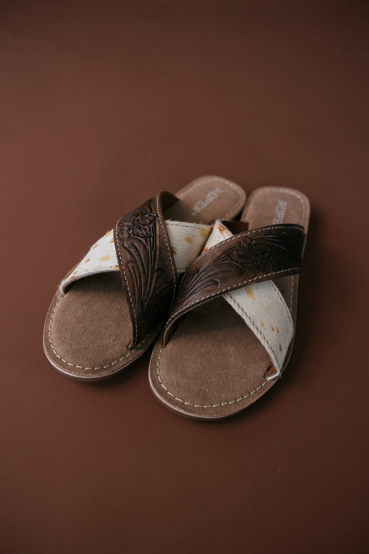 Pair of brown sandals with white soles on a brown background