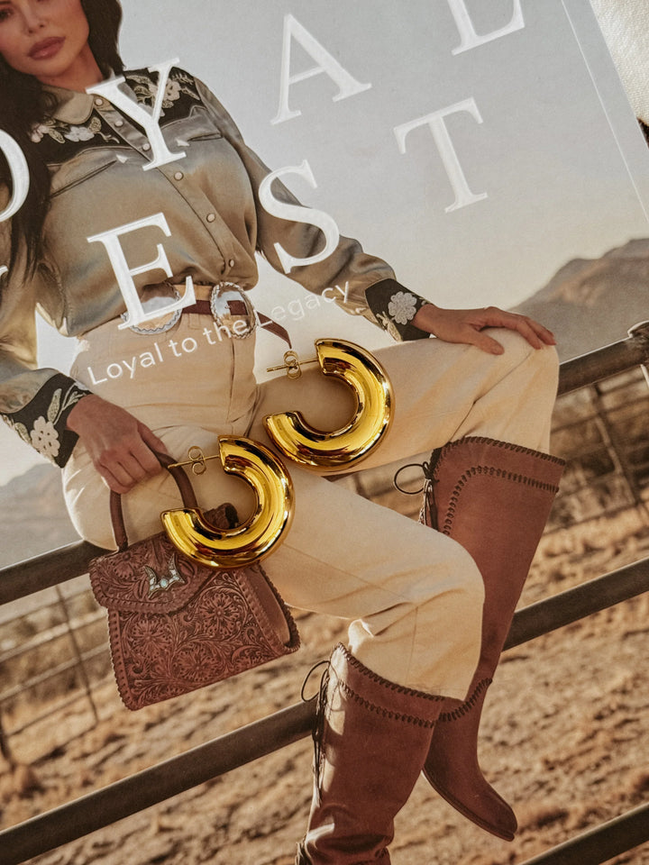 Gold western hoop earrings on cowgirl fashion magazine with boots, tooled purse and rodeo outfit.