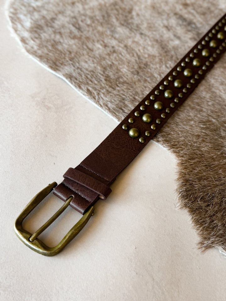 Brown leather belt with brass studs and buckle on a textured surface