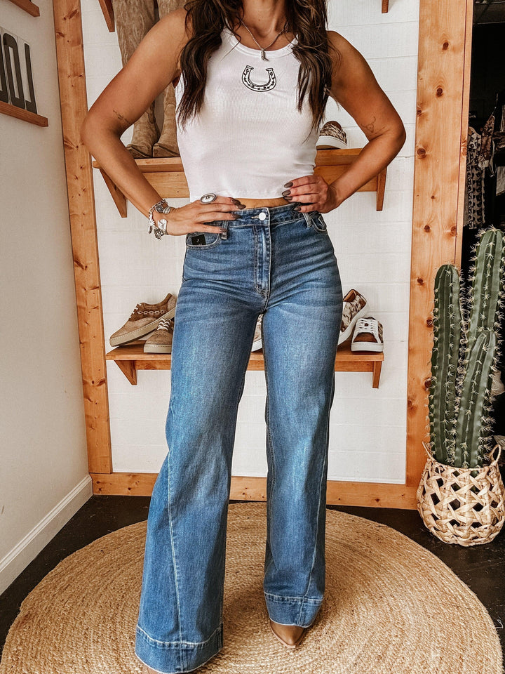 Woman wearing a white crop top with horseshoe graphic and high-waisted flare jeans in a western boutique setting.