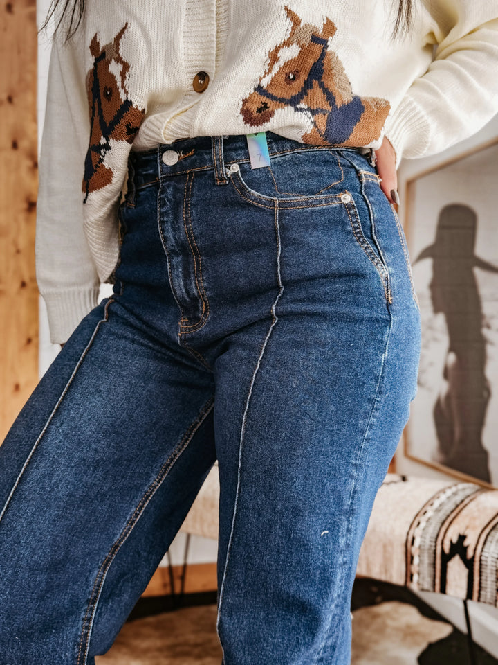 Woman in high-waisted western jeans and cream sweater with horse print, boho decor background