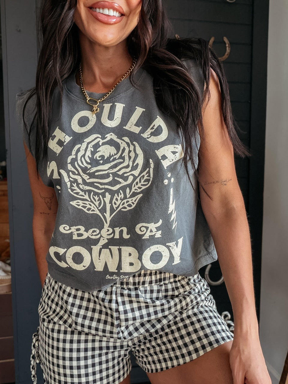 Woman wearing a sleeveless graphic shirt with text and checkered shorts.