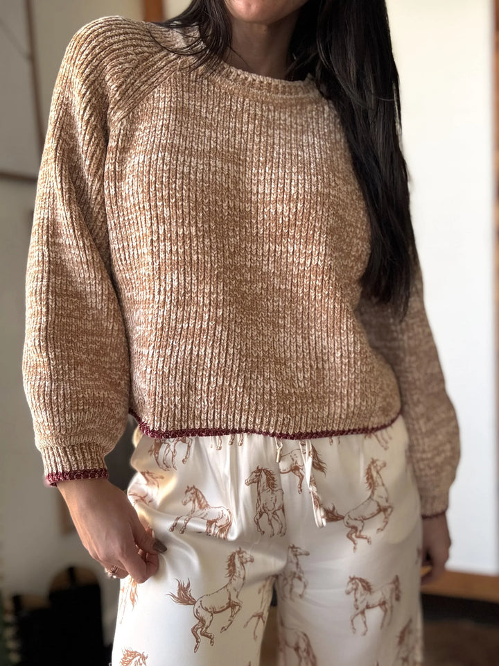 Person wearing a beige sweater and patterned pants indoors