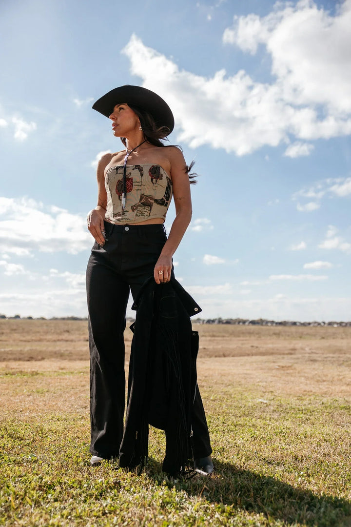 Woman in western boho outfit with black cowboy hat, tube top, wide-leg pants in open field
