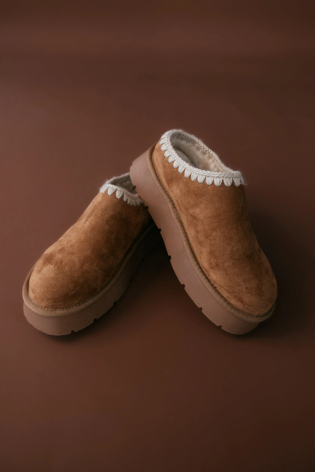 Pair of brown slippers with white fur lining on a brown background
