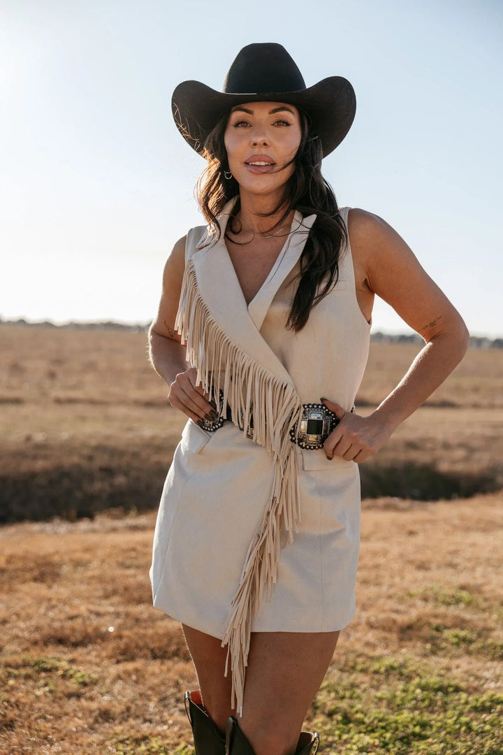 Woman in cowgirl hat and fringed western dress with concho belt standing outdoors