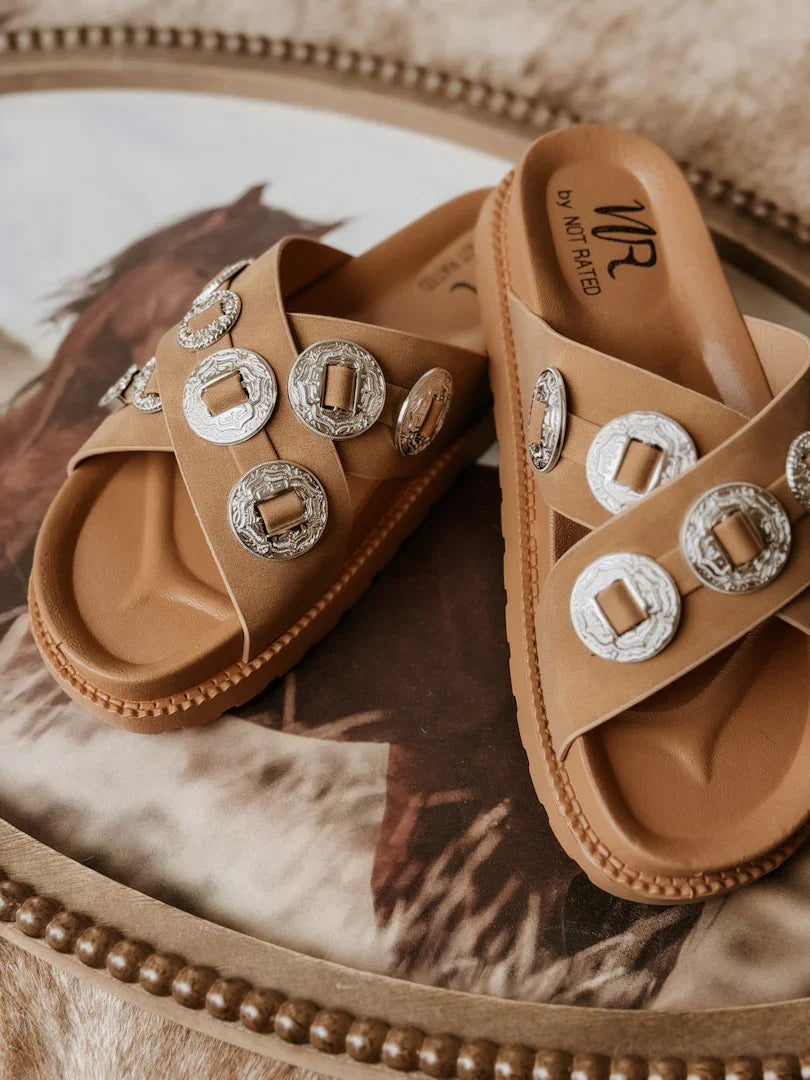 Tan sandals with decorative buckles on a patterned surface