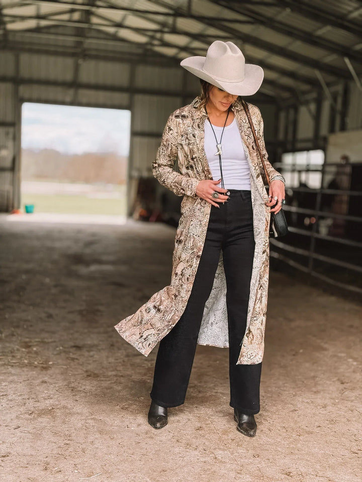 Woman in cowgirl hat, paisley duster, white top, and black pants in barn, western fashion