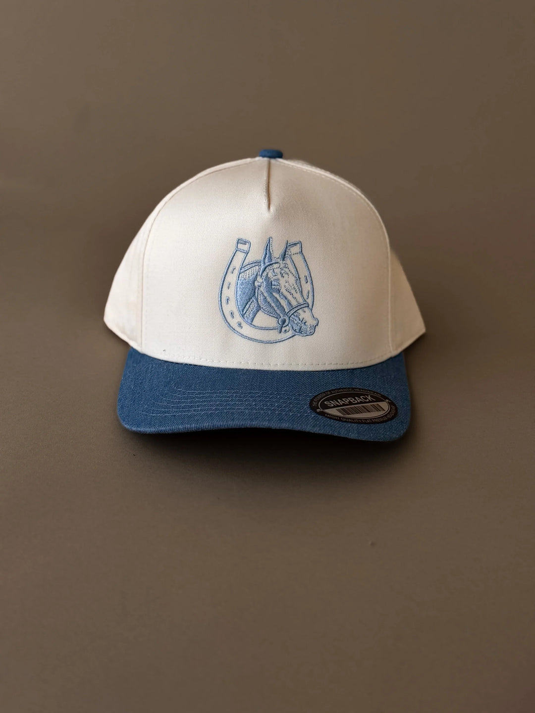 Western snapback hat with blue horse and horseshoe embroidery, cream crown, blue brim.