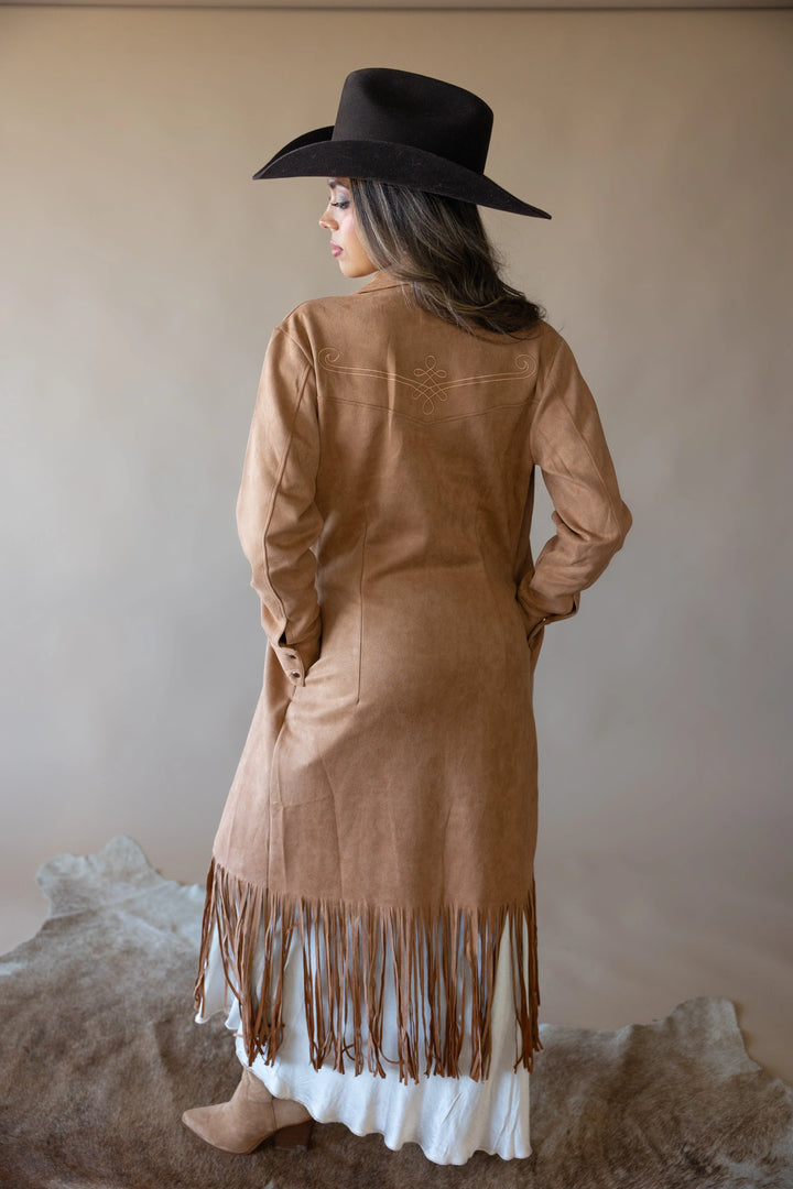 Woman in suede fringe western duster coat, black cowboy hat, and boots on cowhide rug