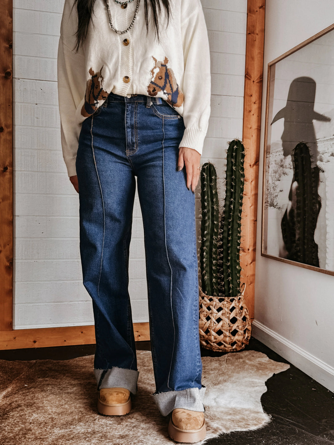 Woman wearing western boho jeans, horse print cardigan, and boots, styled with a cactus decor.