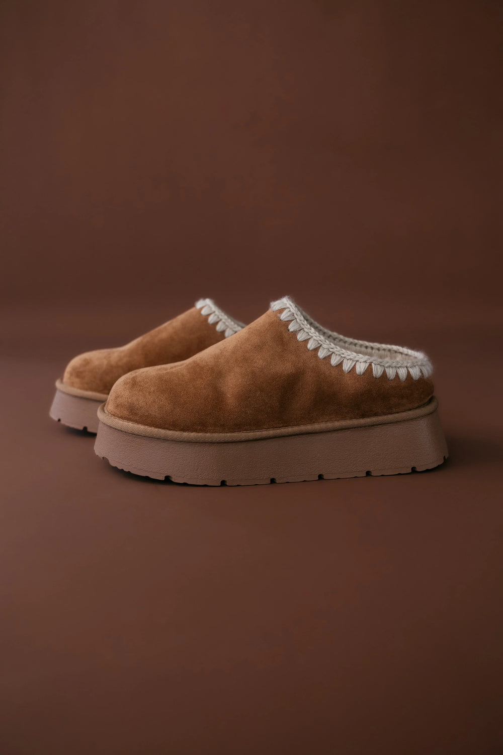 Pair of brown slippers with white trim on a brown background