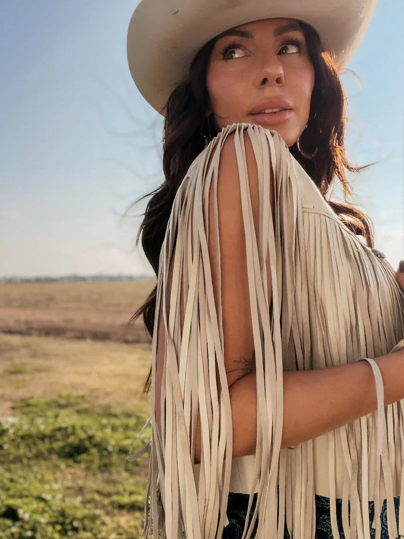 Woman in cowgirl hat and fringe western top standing outdoors in boho rodeo style
