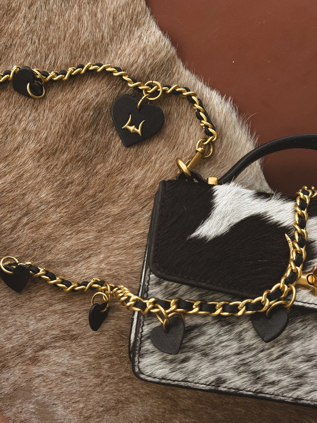 Black and white cowhide handbag with gold chain strap on a brown fur surface