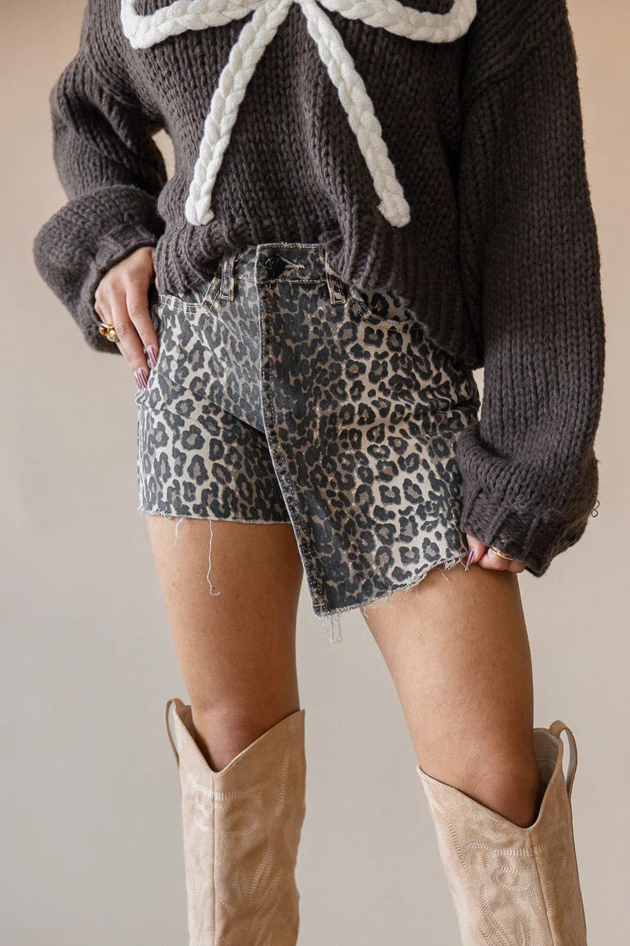 Person wearing a dark sweater with a white bow, leopard print shorts, and beige boots on a neutral background