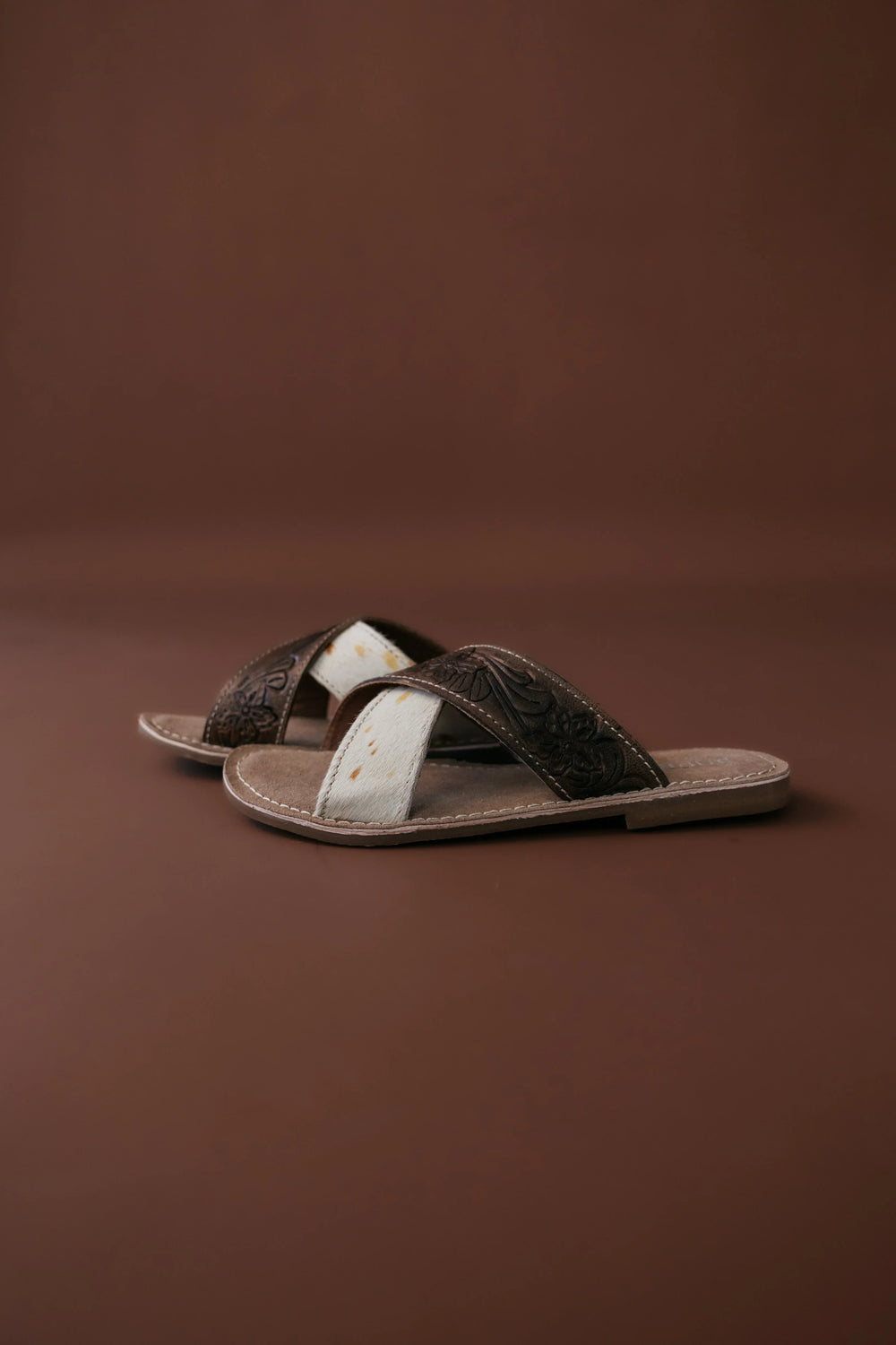 Pair of brown sandals with white soles on a brown background