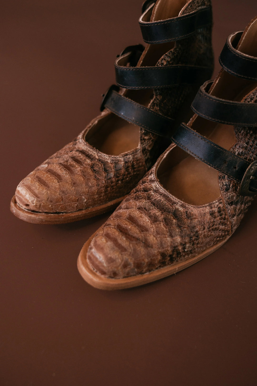 Pair of brown sandals with black straps on a brown background