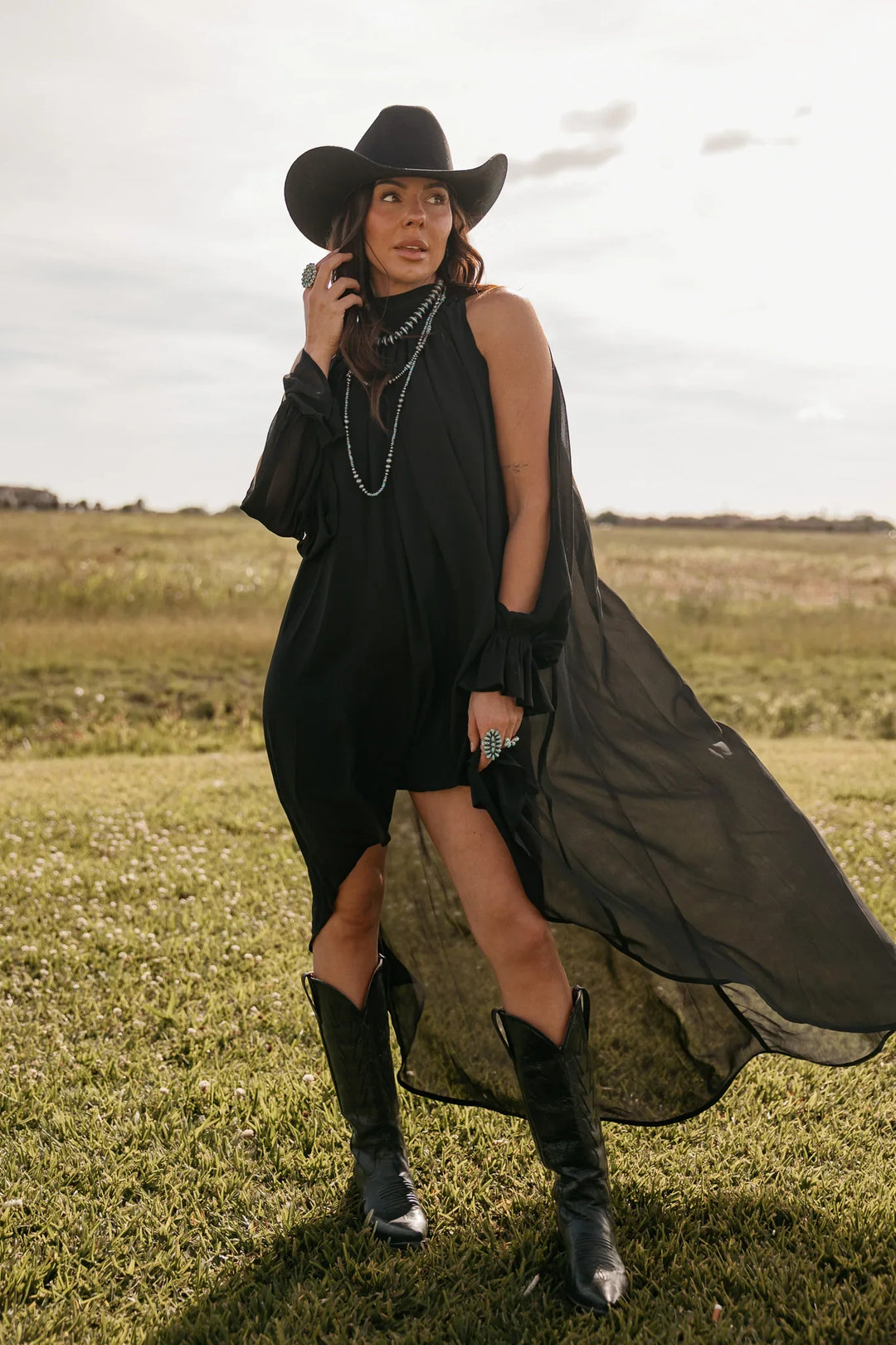 Woman in a black dress and cowboy hat standing in a field
