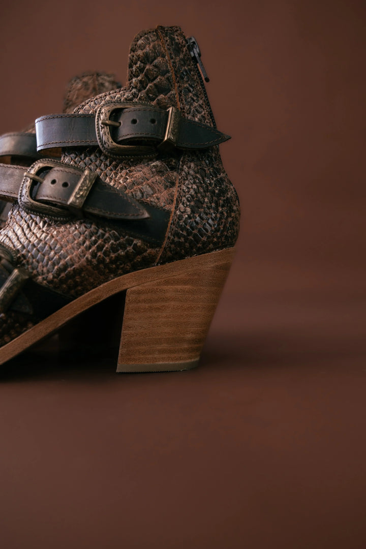 Brown leather boot with decorative buckles on a brown background