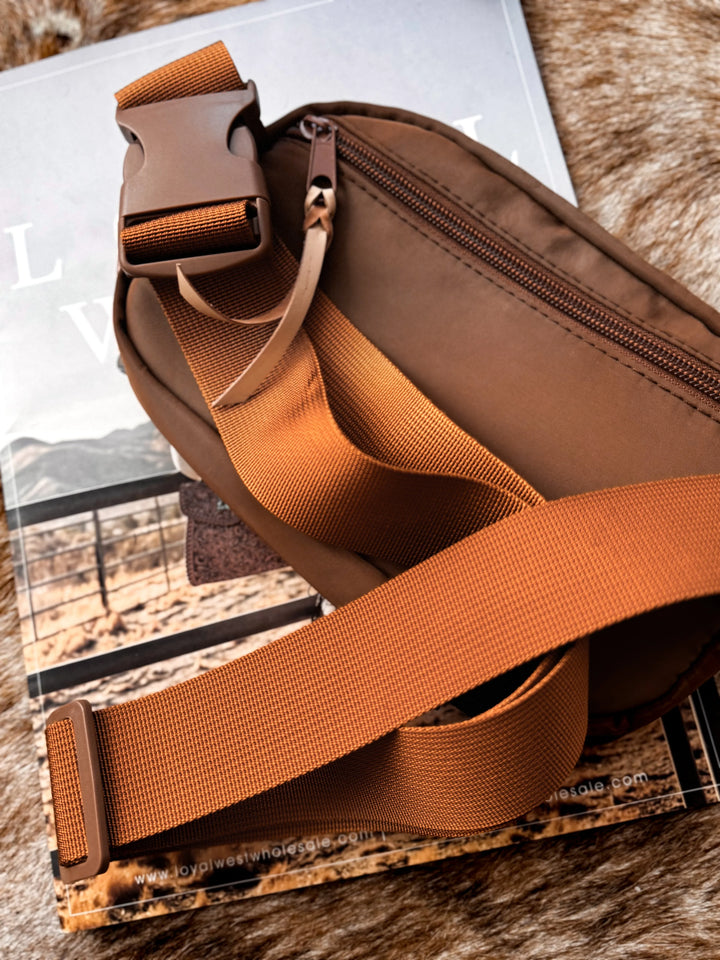 Brown sling bag with a strap on a textured surface