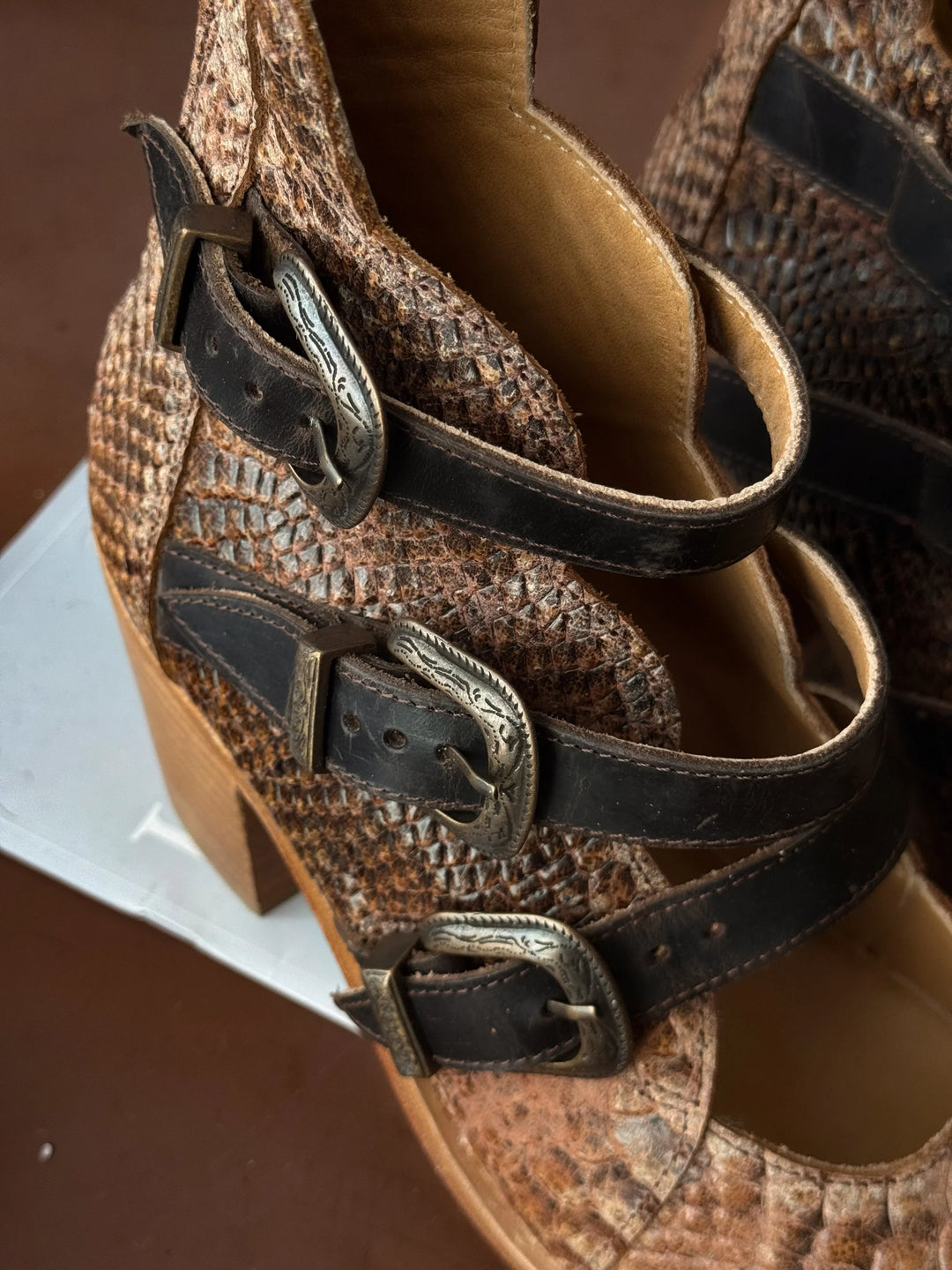 Close-up of a brown leather shoe with decorative buckles on a brown background