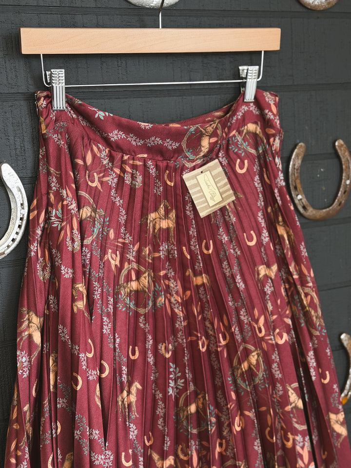 Maroon dress with horse and horseshoe pattern on a hanger against a dark background