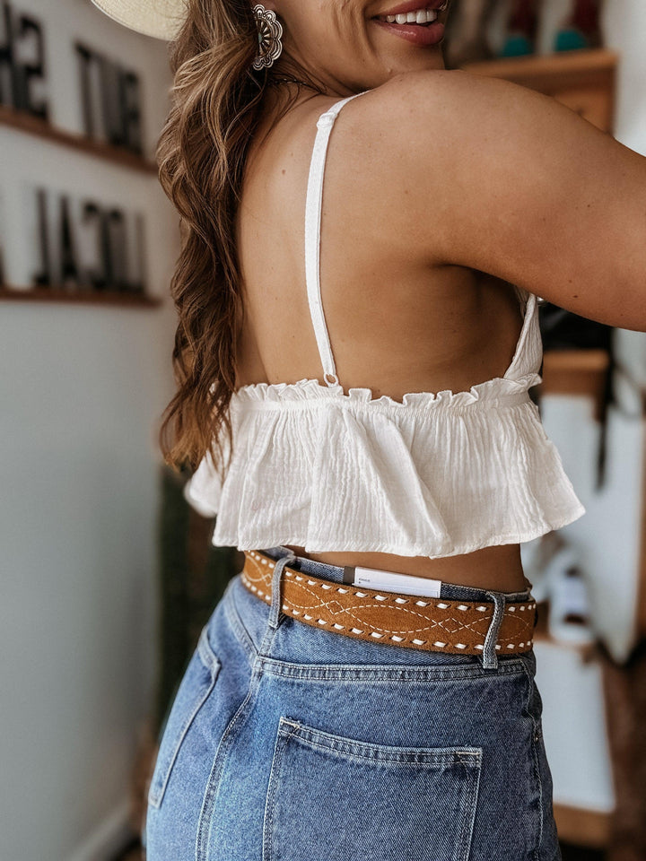 Woman in western boho outfit with white ruffle crop top, high-waisted jeans, and brown belt