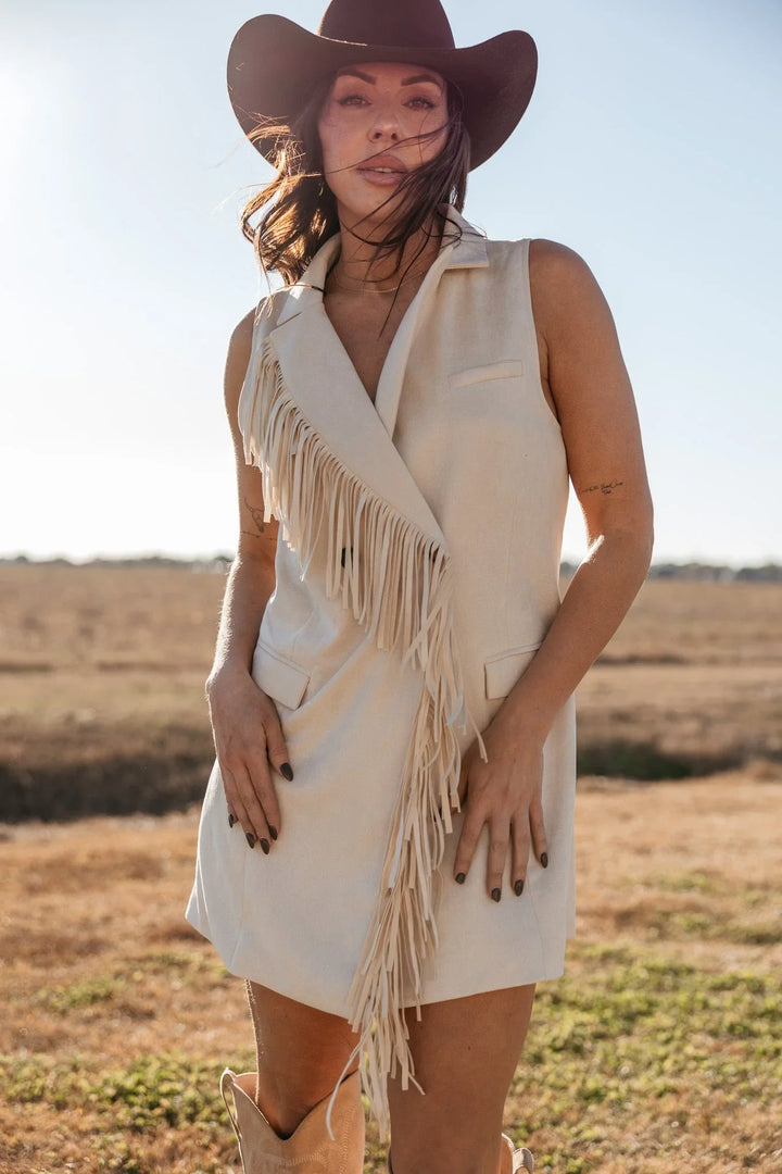 Woman in cream fringe western vest dress and cowboy hat outdoors, cowgirl boho style