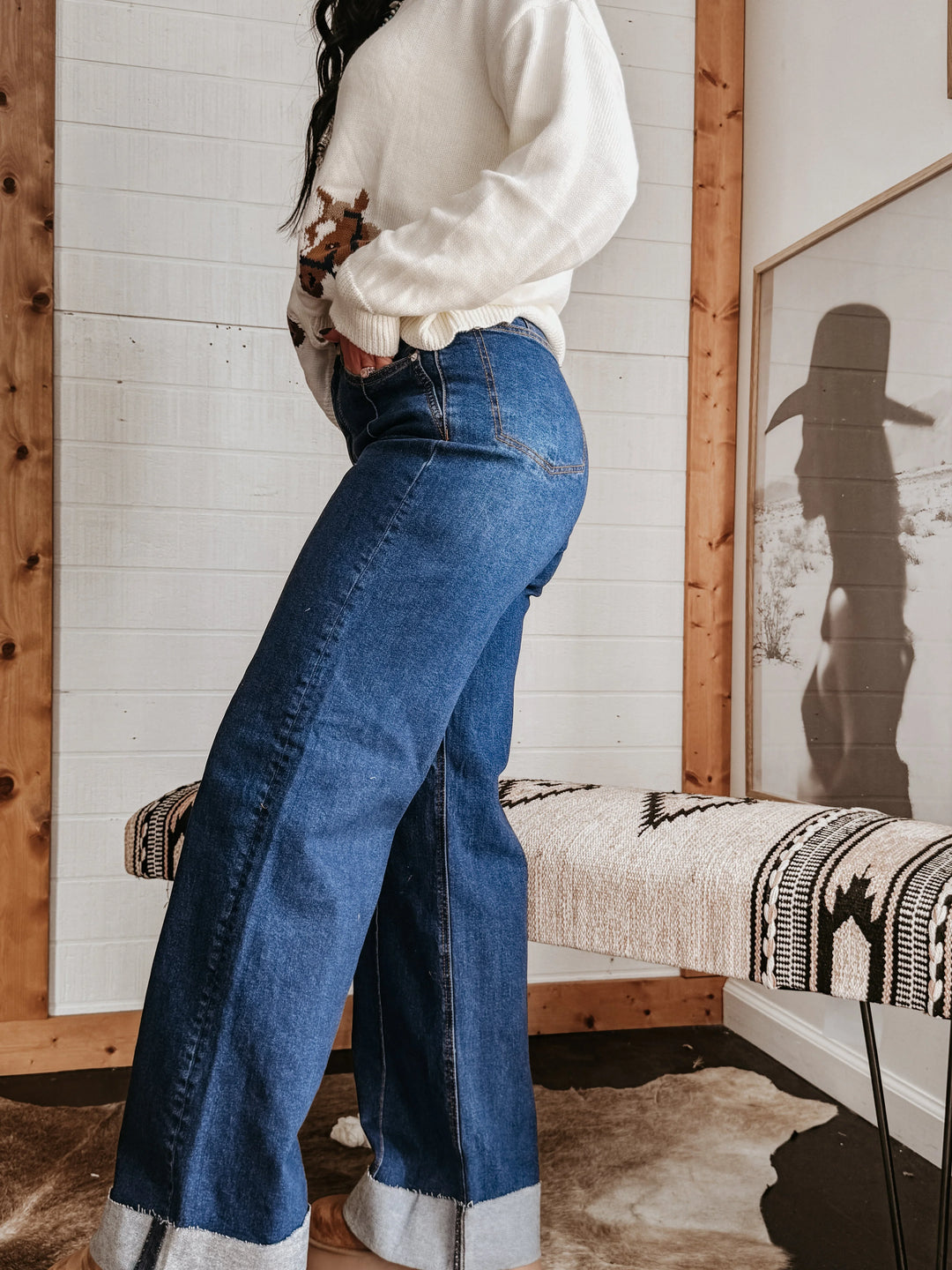 Woman wearing wide leg denim jeans and cow print sweater in western boho styled room