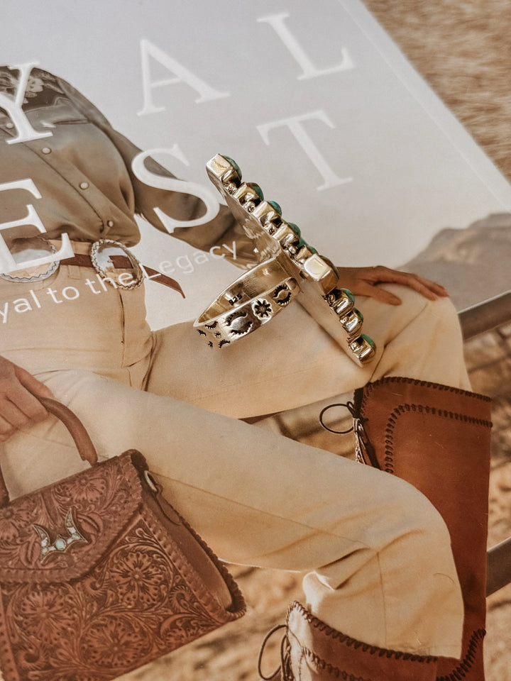 Western silver turquoise ring on magazine with cowgirl outfit, leather purse, and boots