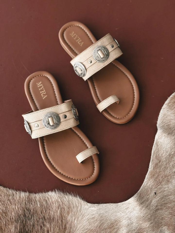 Pair of beige sandals with metallic buckles on a brown surface