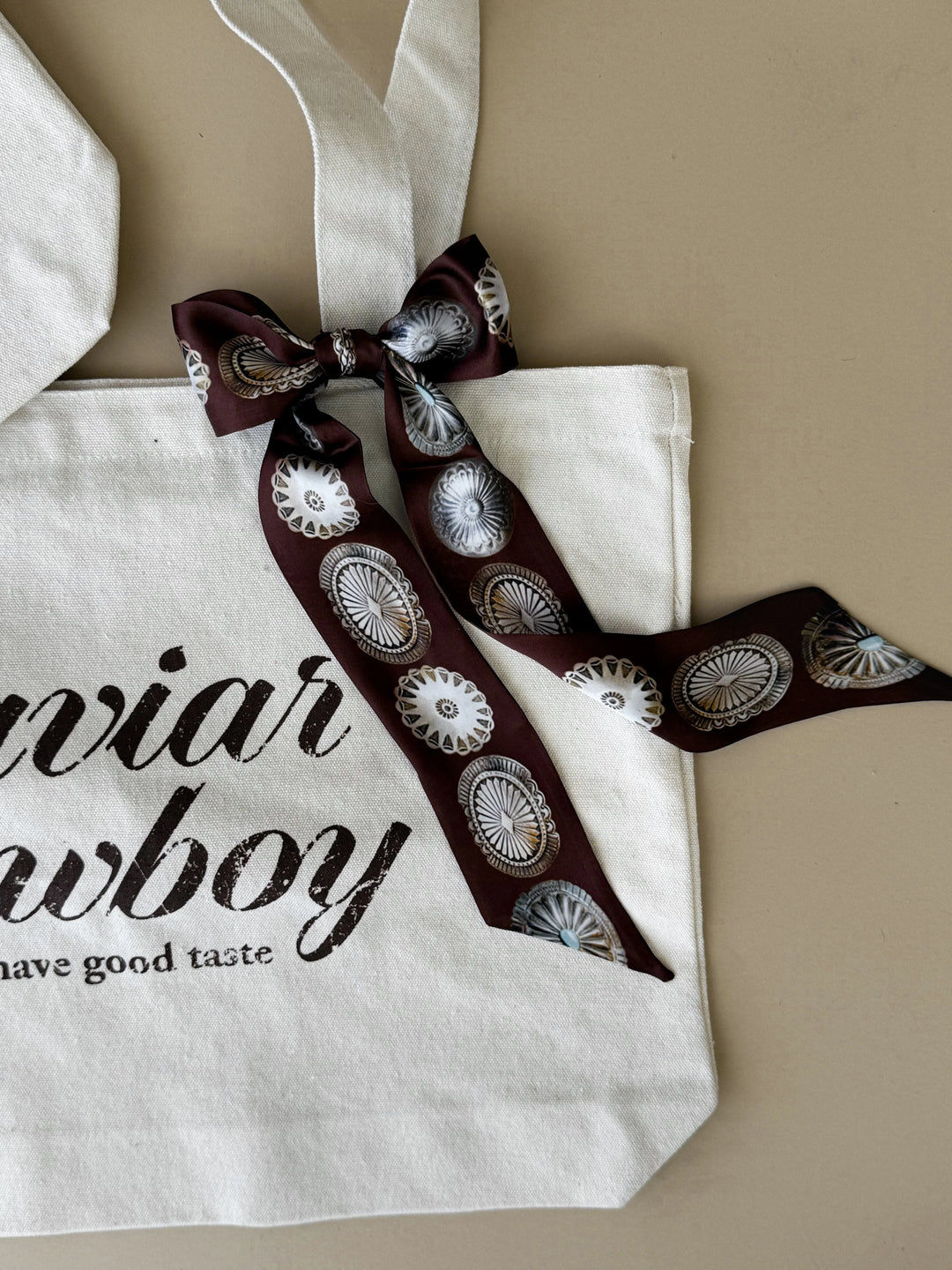 Decorative ribbon with cowboy design on a white tote bag with text.