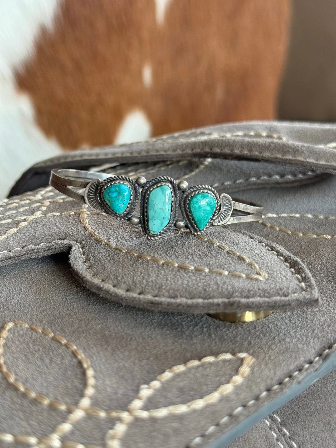 Turquoise silver western cuff bracelet on stitched gray suede with cowhide background