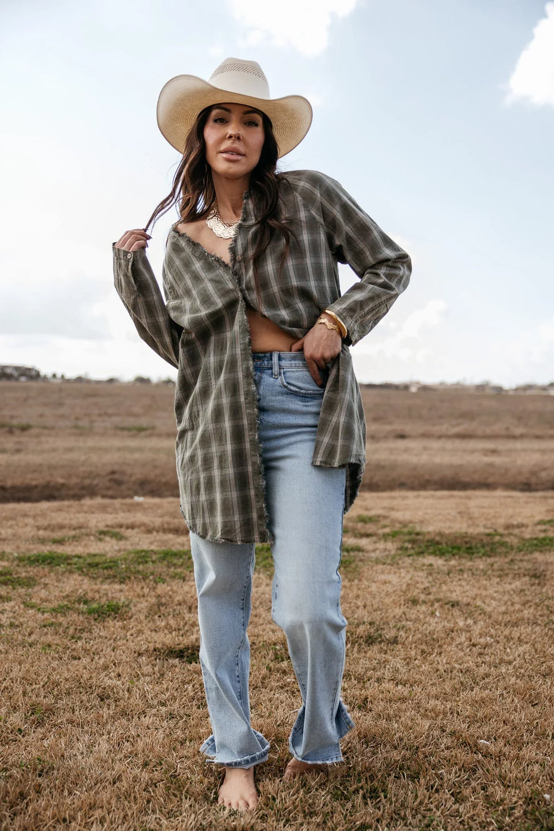 Woman in western boho outfit with plaid shirt, light jeans, and cowboy hat outdoors