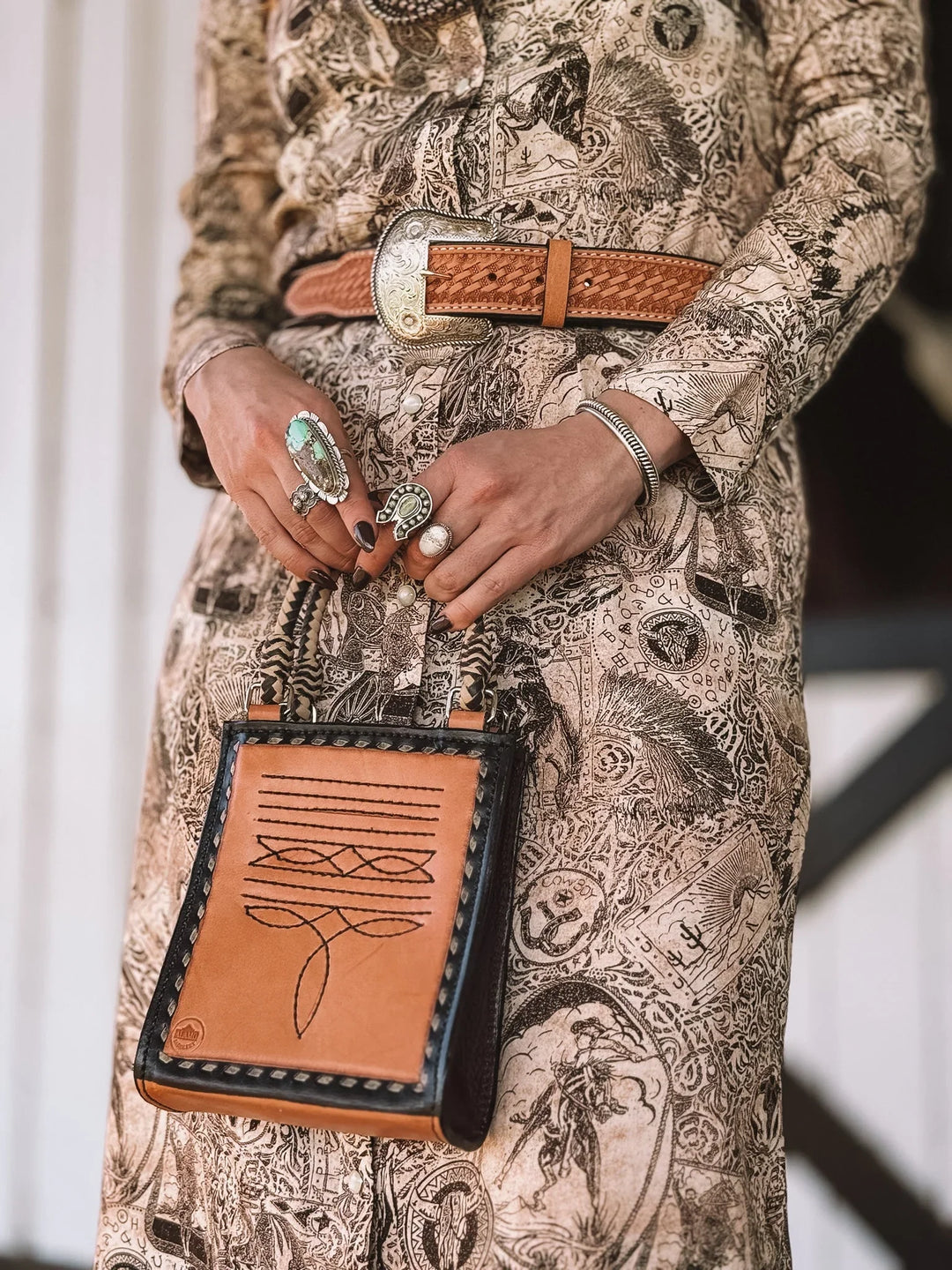Western boho outfit with tooled leather belt, graphic dress, turquoise rings, and stitched purse