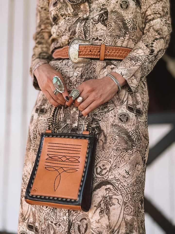 Western boho outfit with tooled leather belt, graphic dress, turquoise rings, and stitched purse