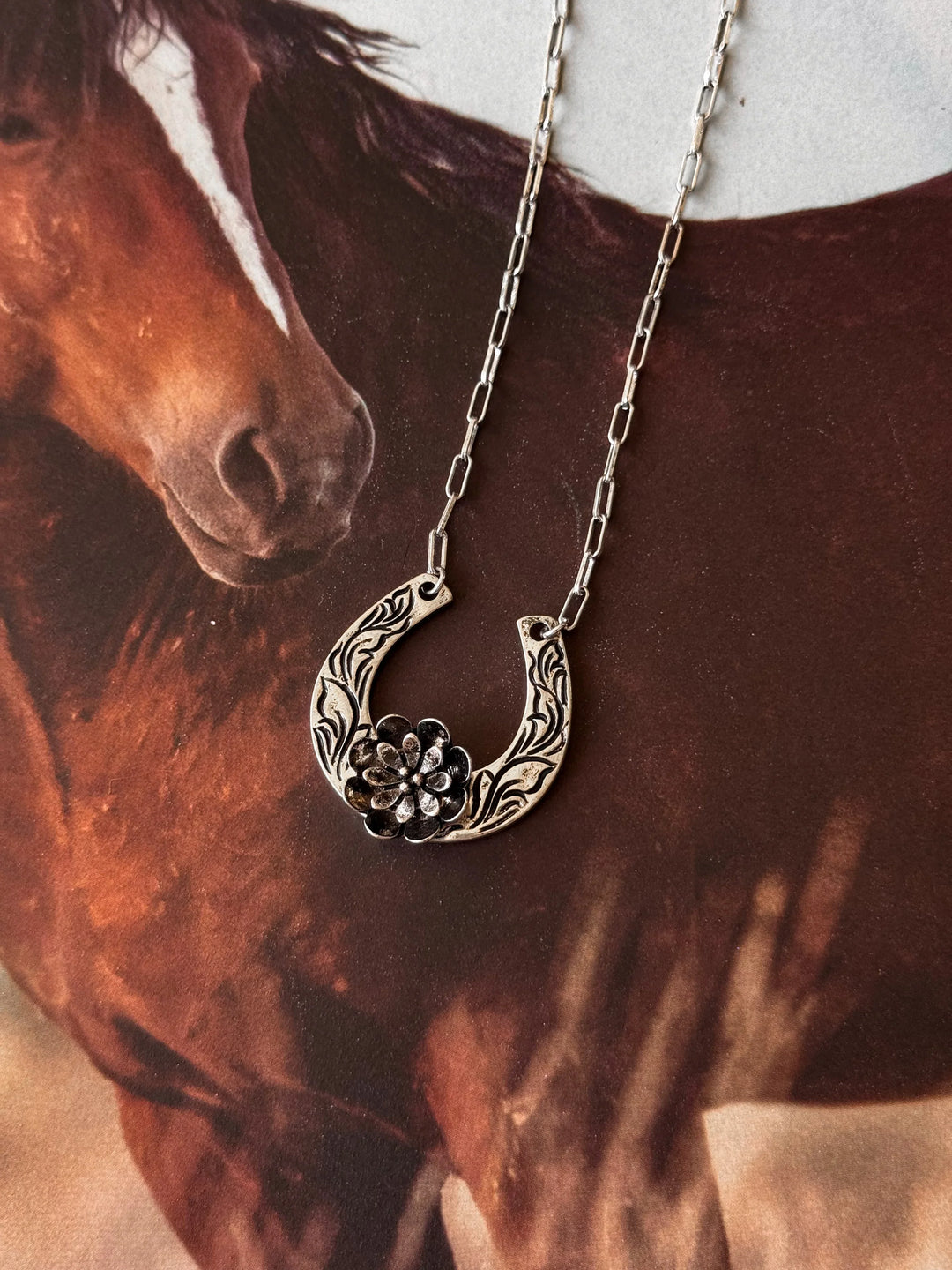 Horseshoe necklace with floral design in front of a horse