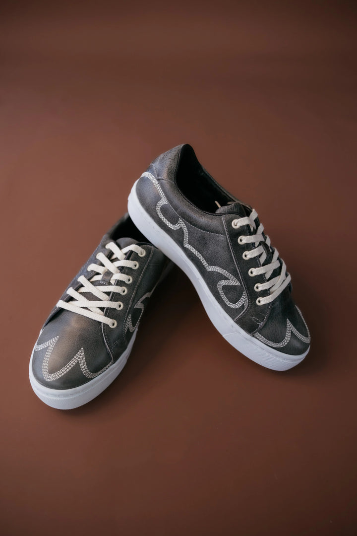Western black sneakers with white stitching and laces on a brown background