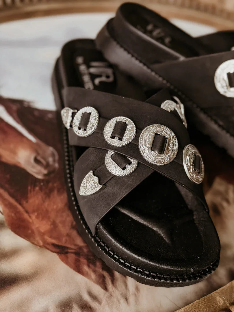 Black sandals with silver buckles on a textured surface