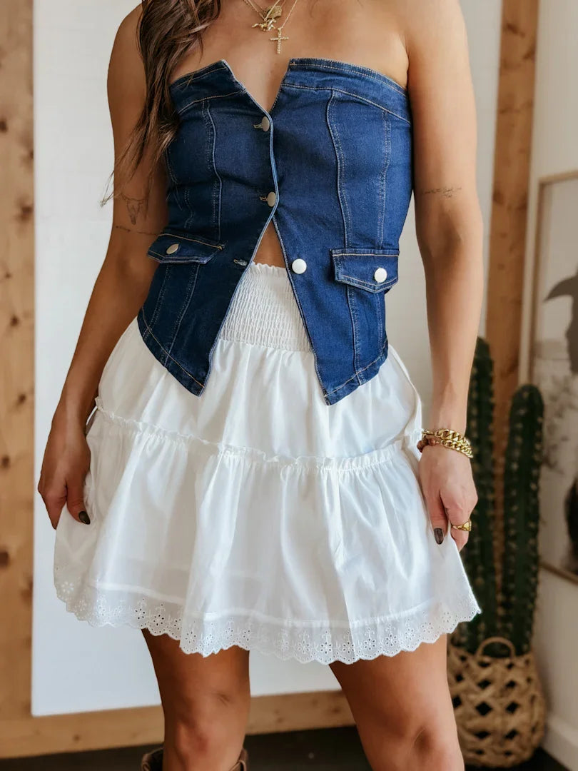 Person wearing a white dress with a denim jacket over shoulders indoors.