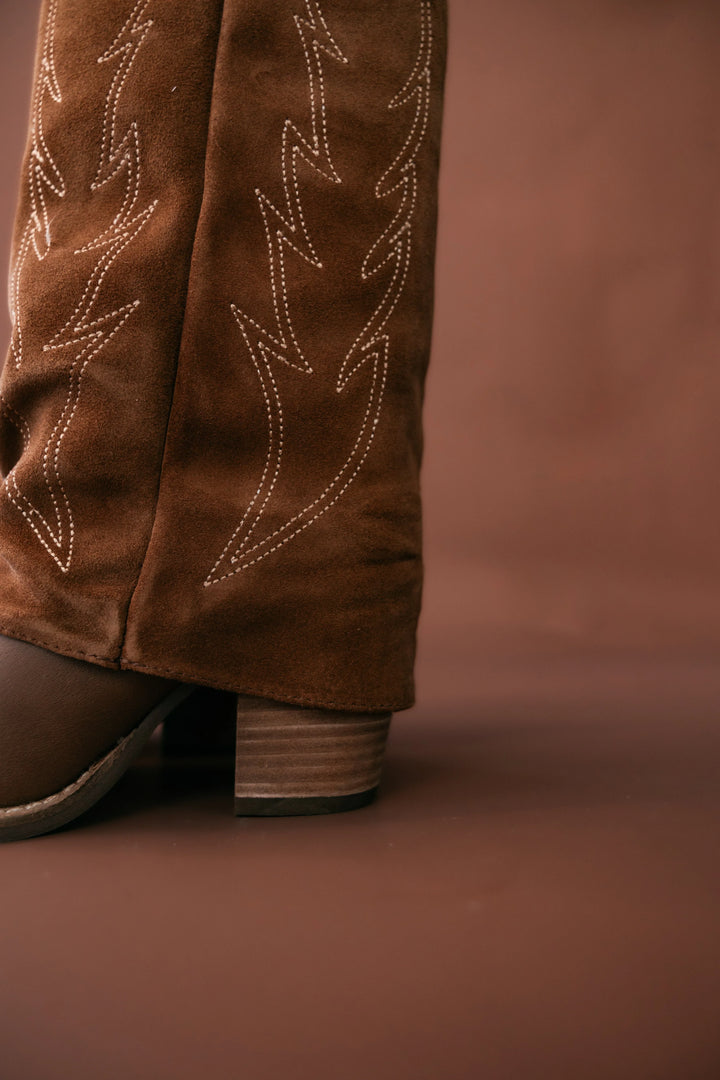 Brown suede boot with decorative stitching on a brown background