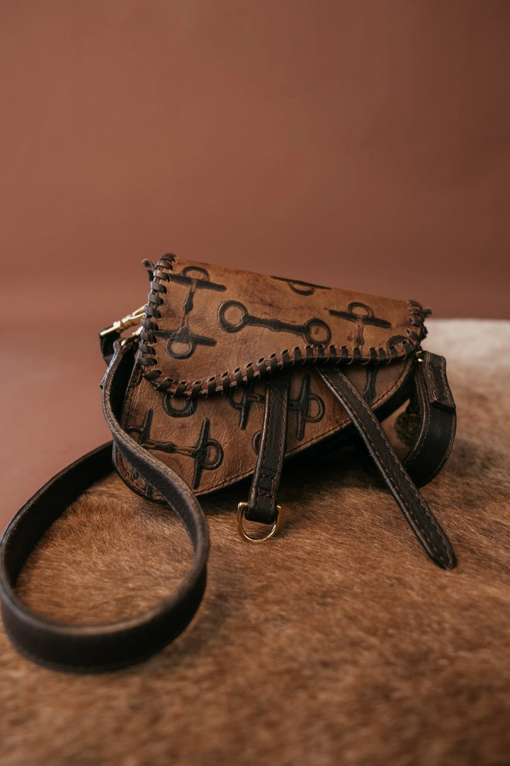 Brown leather handbag with black strap on a brown background