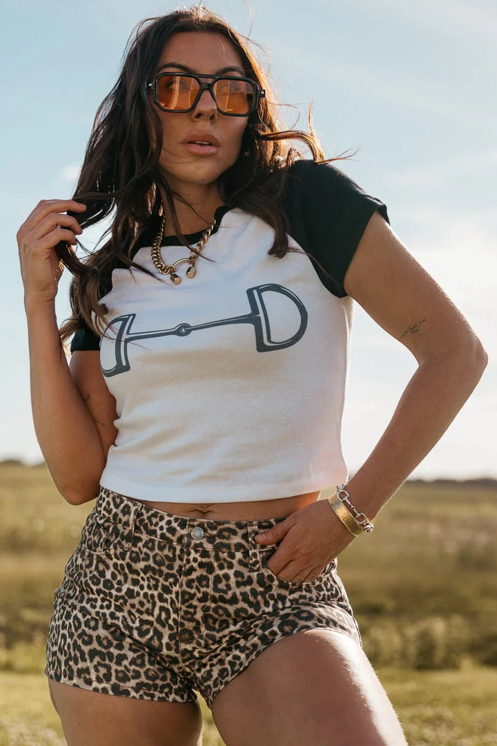 Woman wearing a white crop top with a logo and leopard print shorts in an outdoor setting