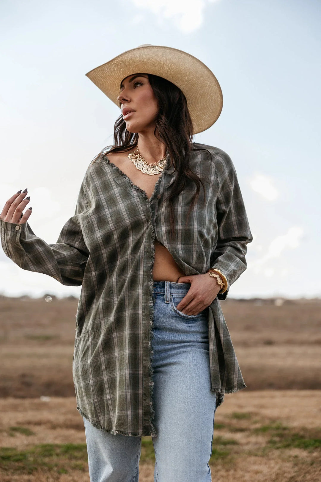 Woman in a straw cowboy hat, plaid western shirt, and distressed jeans outdoors